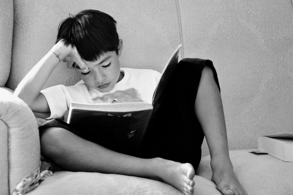 product-management-courses-stock-kid-with-book-2 Kid reading a book in black and white on the couch