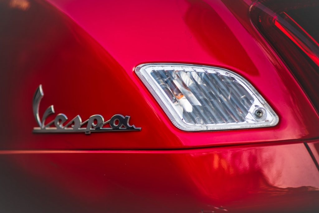logo5 "Vespa" written in silver on the side of red scooter