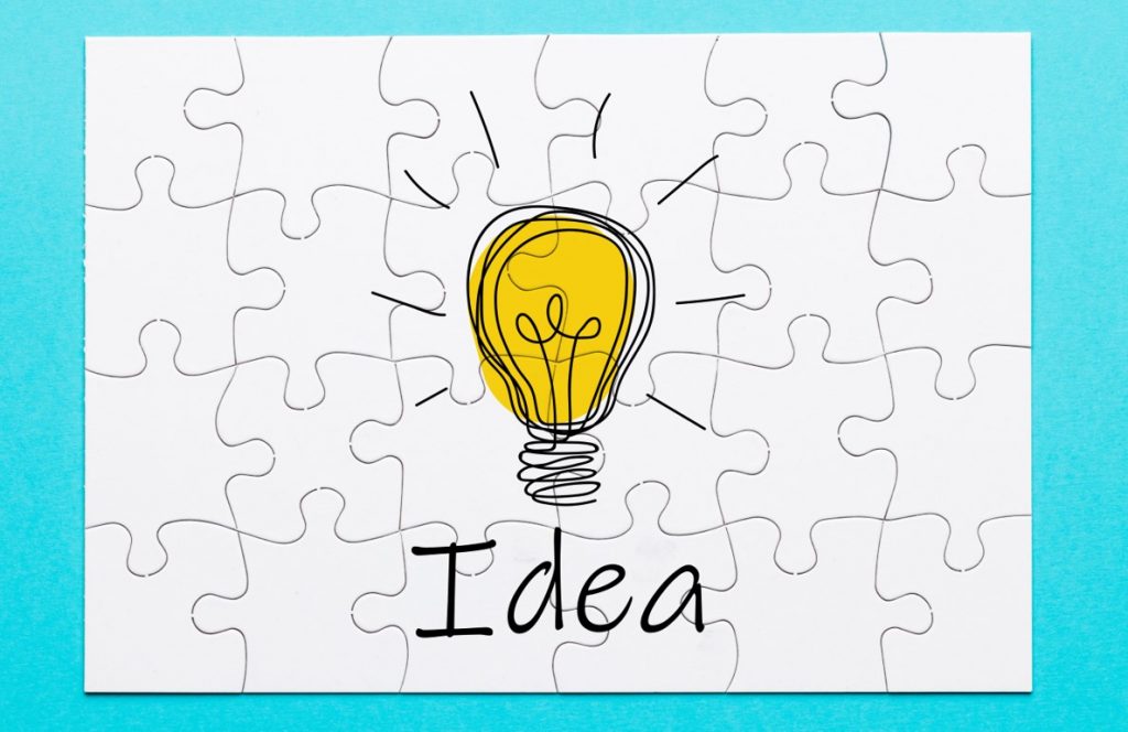 idea Lightbulb on with "idea" written under it in a white puzzle background with teal outline