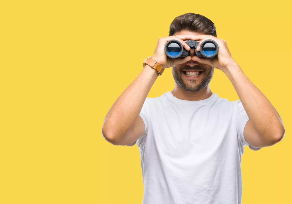 Young,Handsome,Man,Looking,Through,Binoculars,Over,Isolated,Background,With